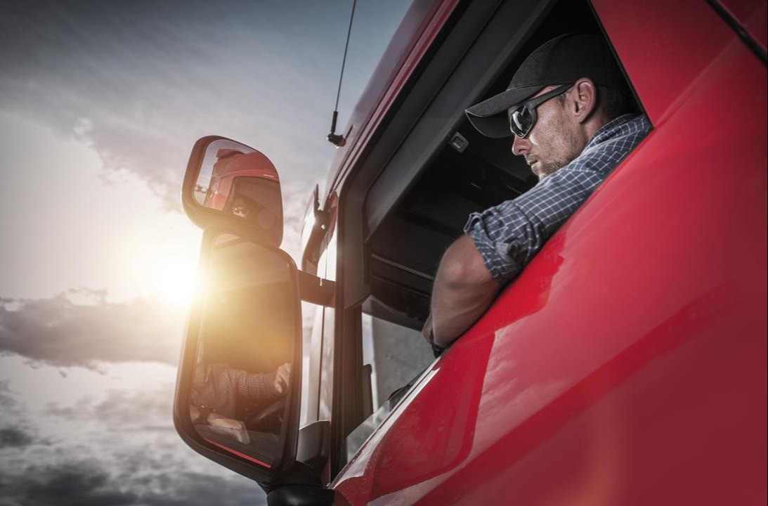 kierowca czerwonej ciężarówki wychyla się przez okno w drzwiach